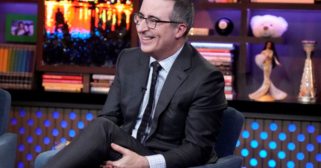 John oliver sitting in with crisscross leg and smiling 