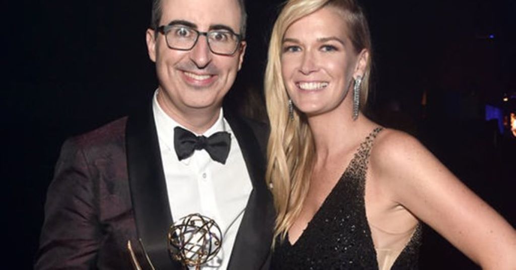 John holding in tux hands of his wife and smiling proving John Oliver is not gay