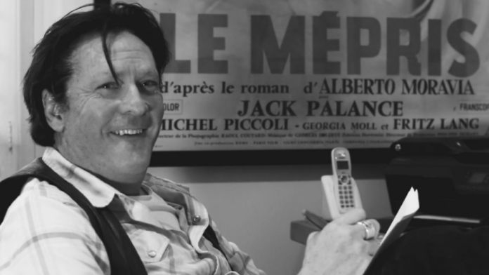 Michael Madsen laughing while holding a newspaper
