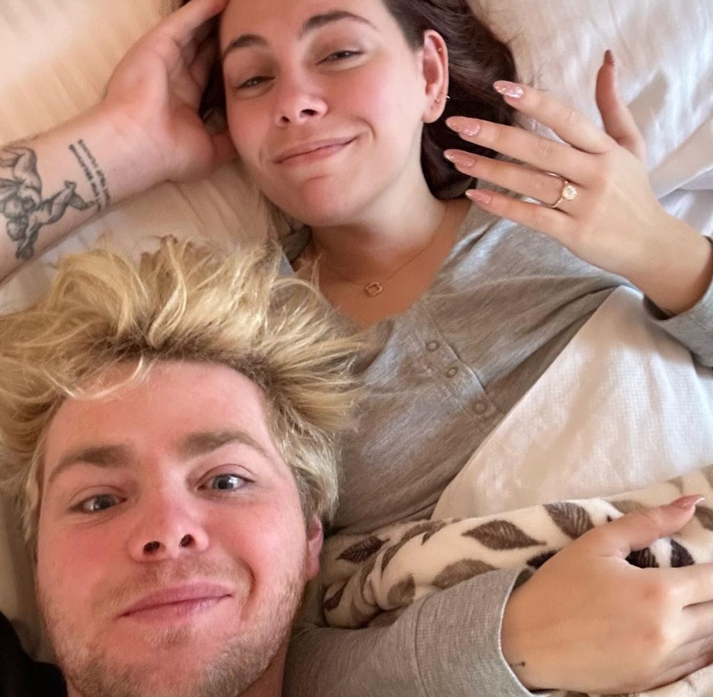 Alex and his fiancé in bed where Kouvr shows her engagement ring 
