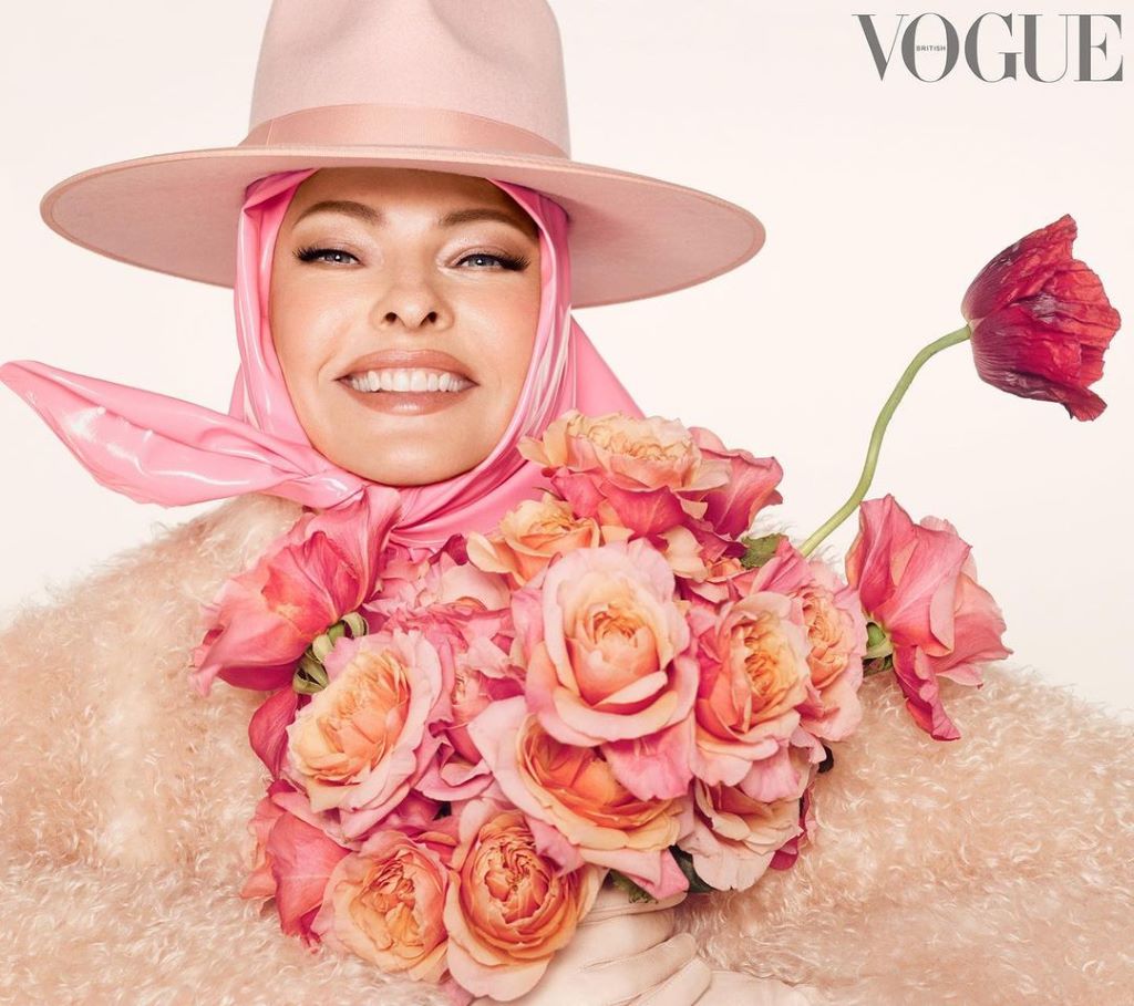 Photo of Linda with an attractive outfit full of flowers and a hat. She has a wide smile in her face. 
