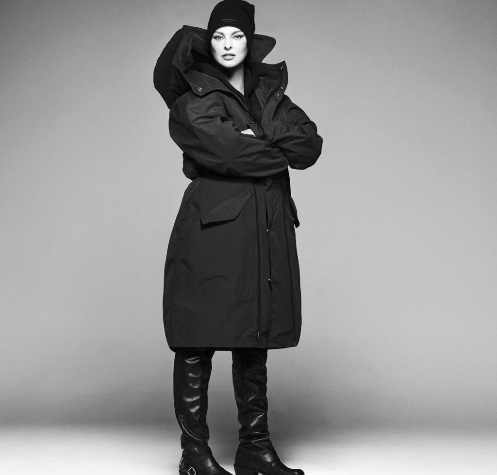 A black and white image of Linda Evangelista. She is wearing a long jacket and black boots.