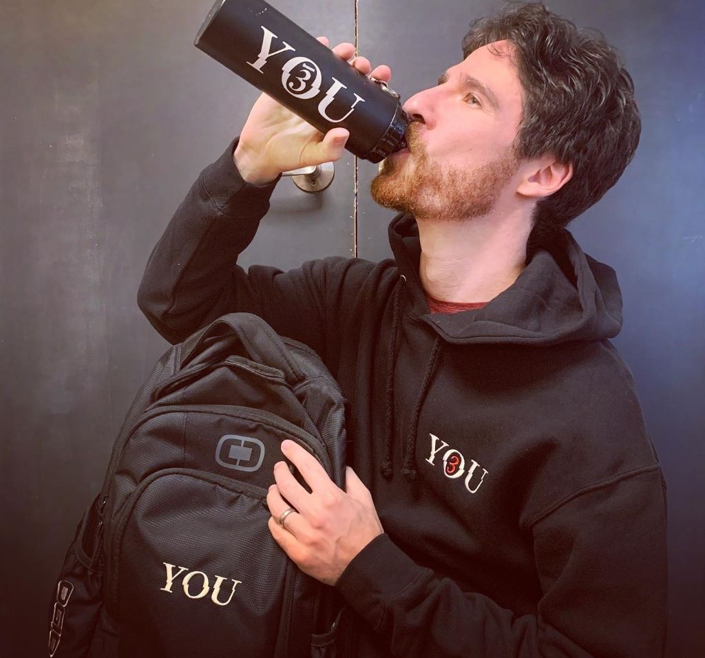 Ben Mehl drinking from bottle and holding bag with You written