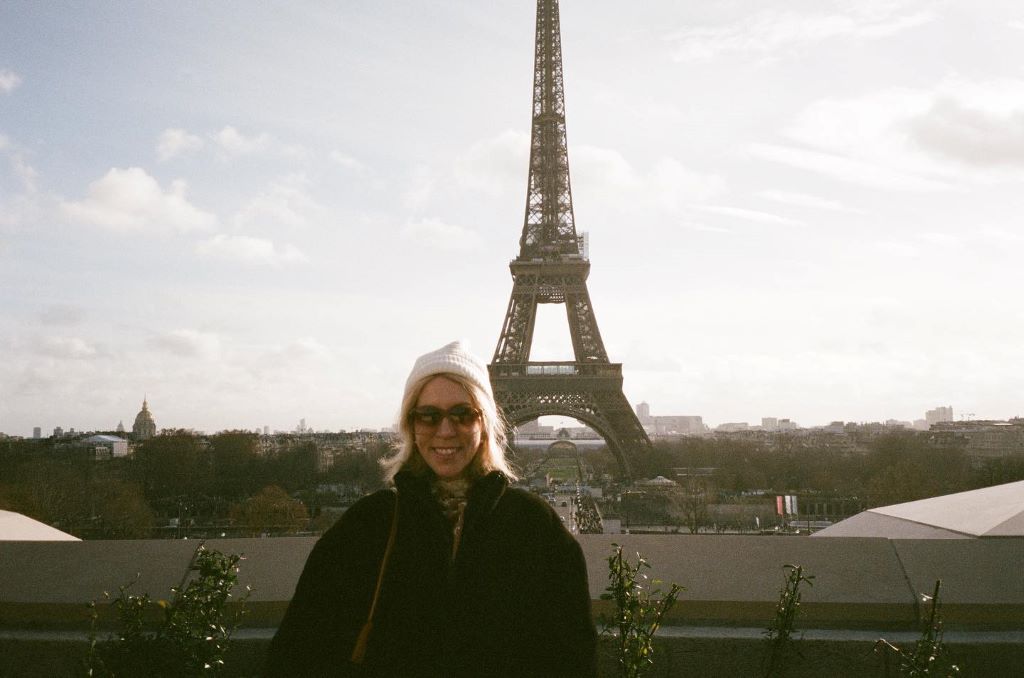smiling brightly with the Eiffel Tower behind her in the background,