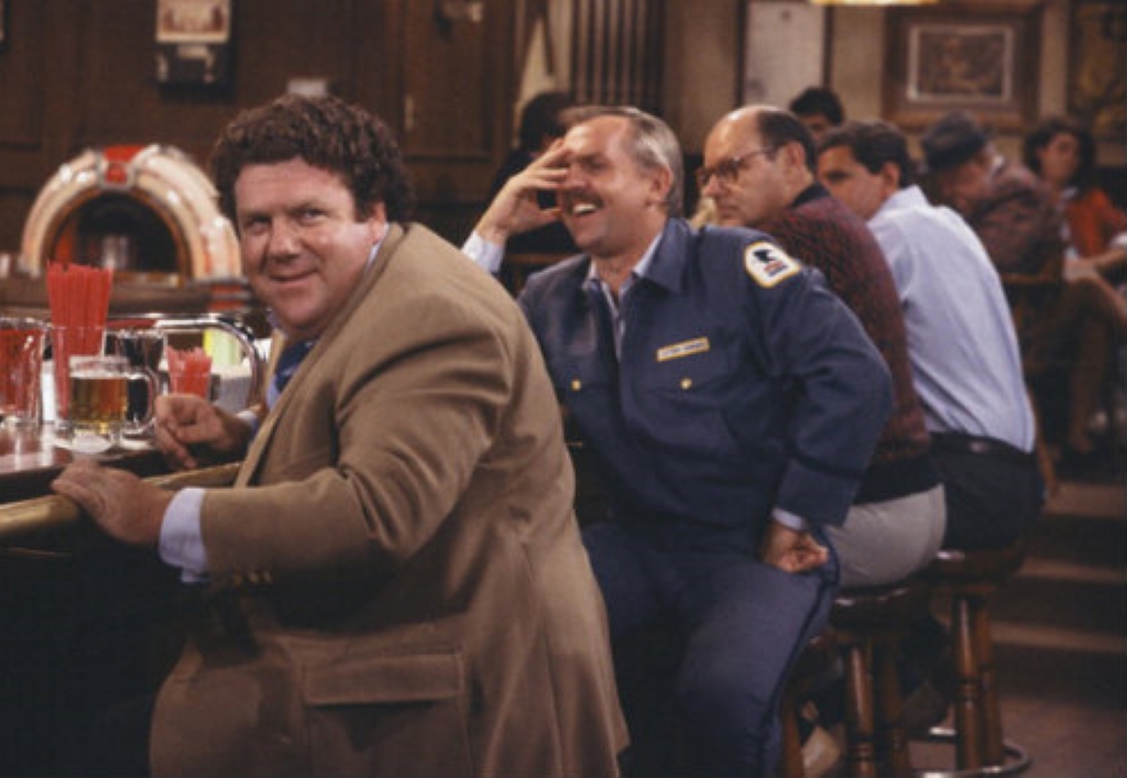 A group of people are sitting and laughing with one another in The Cheers Legacy: Season 3