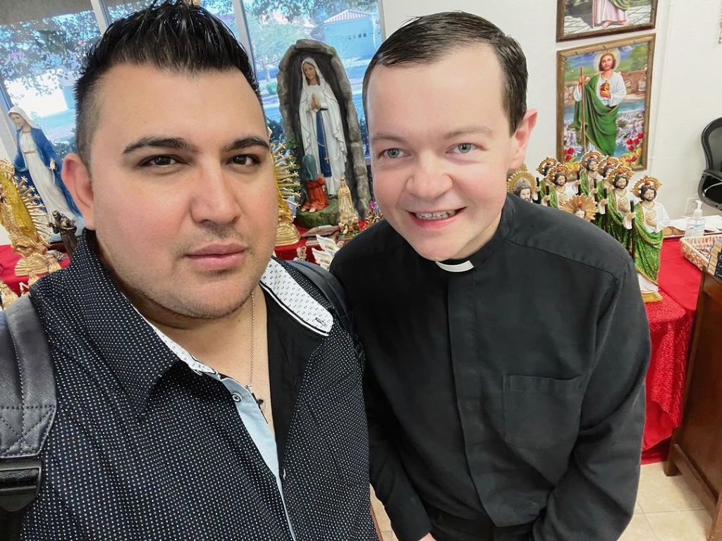 Padre with is fan talking a selfie in his priest dress.