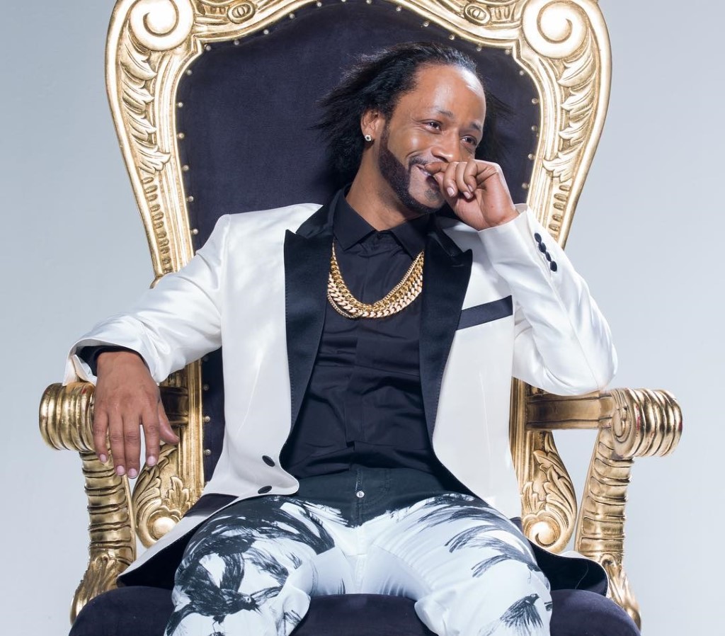 Katt Williams siting on a throne with white coat.