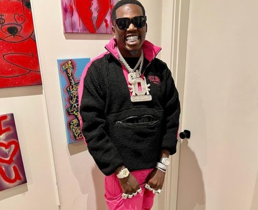 Big Boogie donning a pink and black mixed dress, showcasing his vibrant style and jewelry.