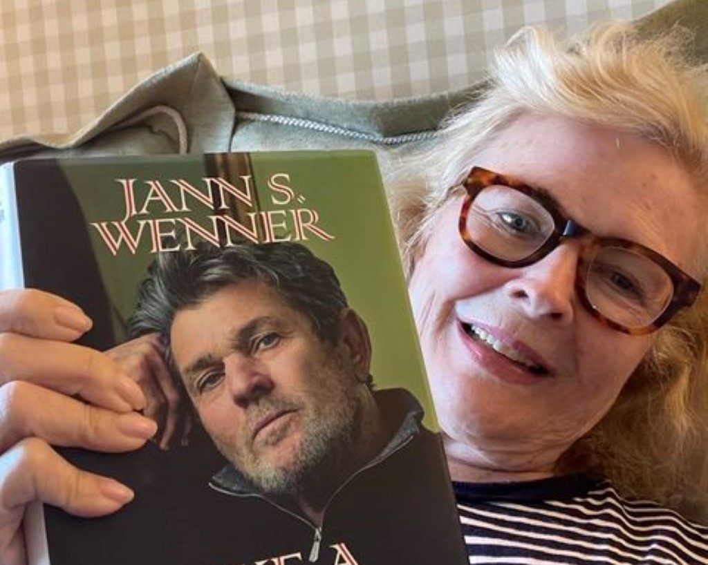 Candice is reading a book by Jann Wenner, lying in her room.