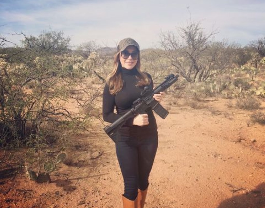Hamill is photographed in a black dress while posing with an automatic rifle.