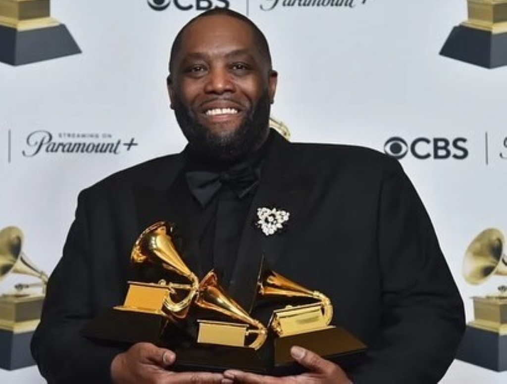 Mike, wearing a black coat, poses with his three Grammy Awards.