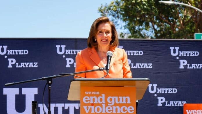 Nancy Pelosi in orange dress giving a speech into a microphone.