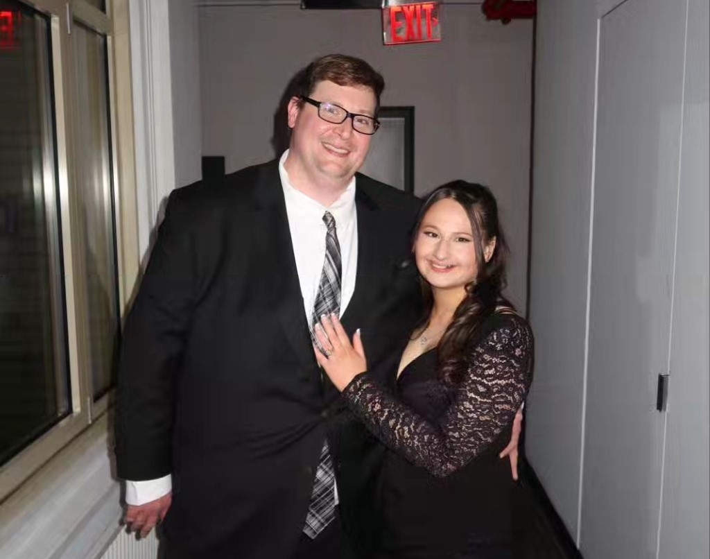 Ryan in a coat and Gypsy in a black dress posing for pictures.